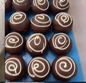 Glossy dark chocolate truffles piped with white chocolate drizzle, cooling in trays at Ricci Chocolates